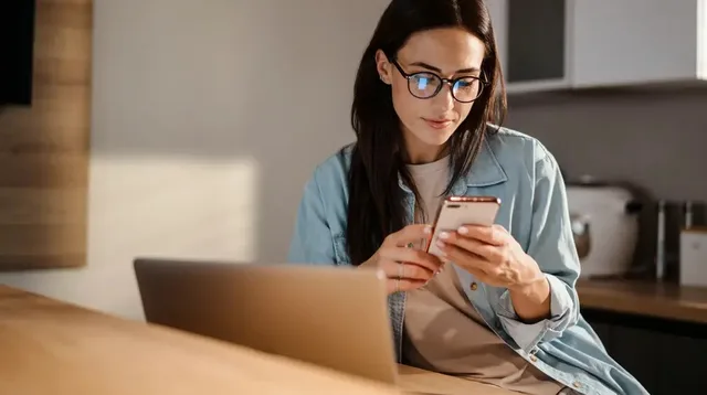 žena s telefonem u notebooku
